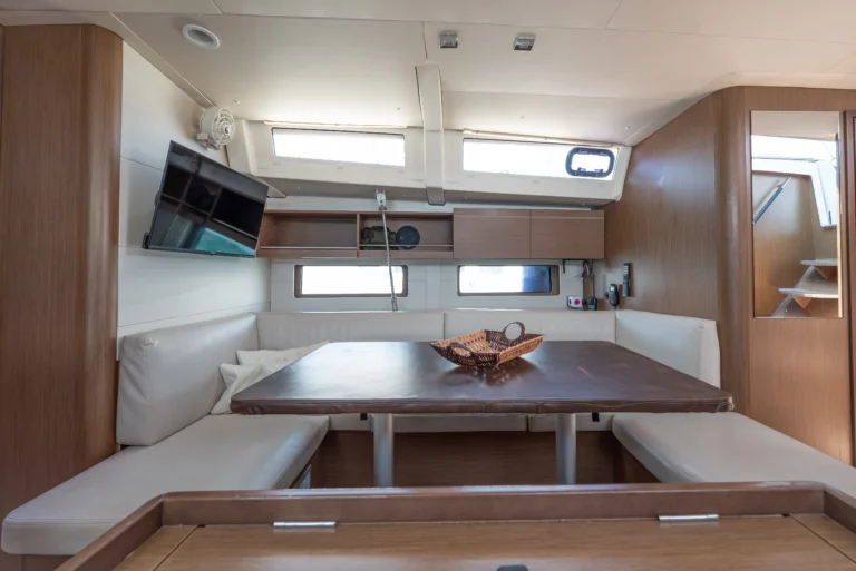 Beneteau Oceanis 46.1 - saloon interior with a TV, dining area, and navigation table for charter in Greece.