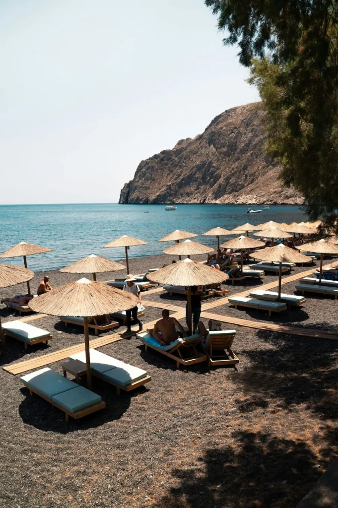 Plaża na Santorini z parasolami słomkowymi i leżakami nad turkusowym morzem