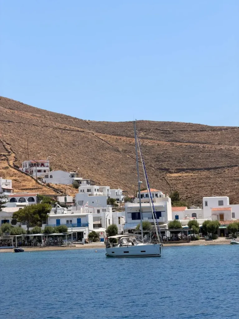 Jacht żaglowy zacumowany przy porcie Merichas na wyspie Kythnos z widokiem na tradycyjną cykladzką zabudowę.